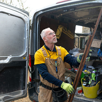 Man in work attire standing next to an open van with tools and equipment inside.