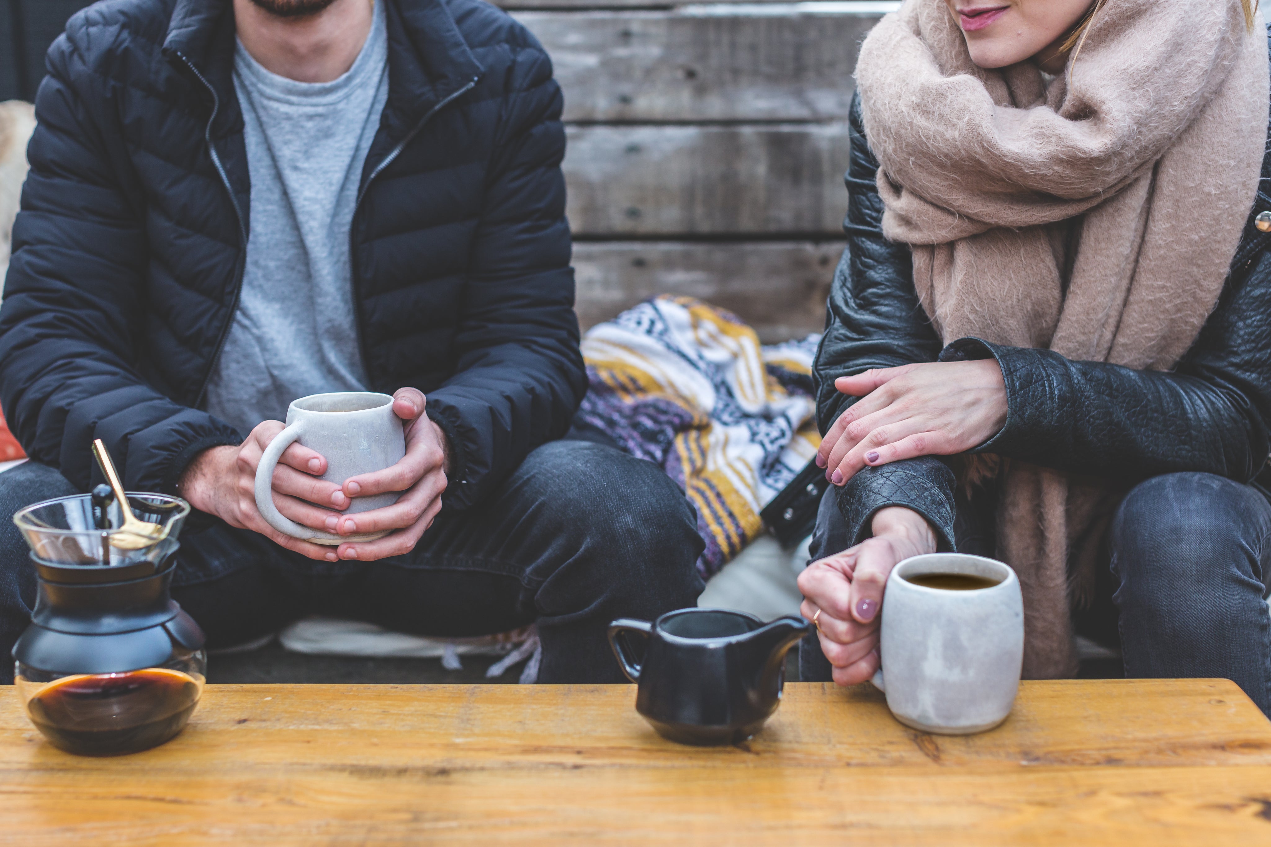 Two people drinking coffee sitting on a bench outside